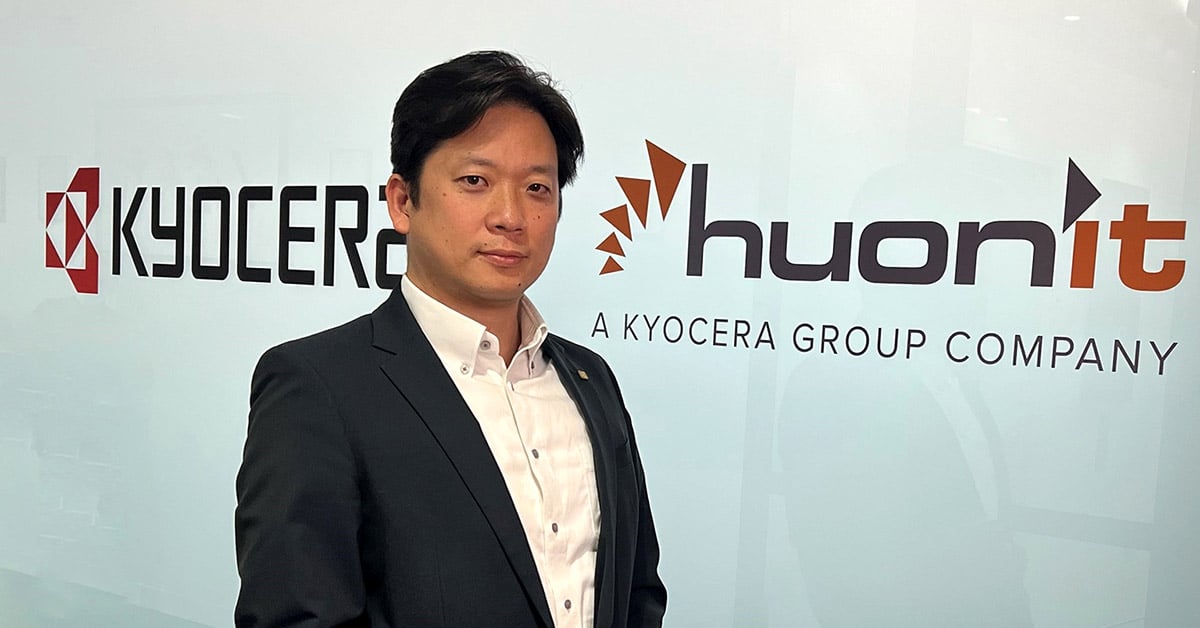 Mr. Motohiro Sato in front of Kyocera and Huon IT logos
